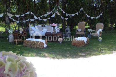 Décoration champêtre avec canapé, fauteuils, bottes de paille et guirlandes dans un jardin verdoyant.