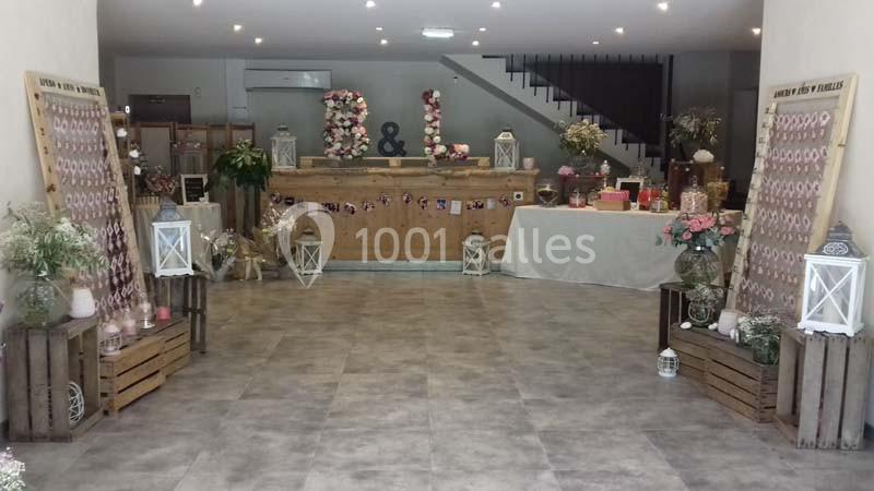 Salle décorée pour un événement avec fleurs, lanternes, panneaux en bois et une table ornée d'objets festifs.