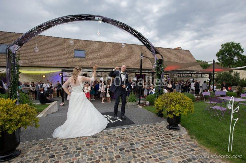 Un couple de mariés danse sous une arche, entouré d'invités dans un jardin lors d'une réception en plein air.