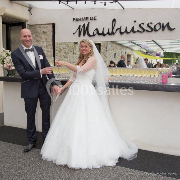 Un couple de mariés souriants trinque devant un bar extérieur à la Ferme de Maubuisson.