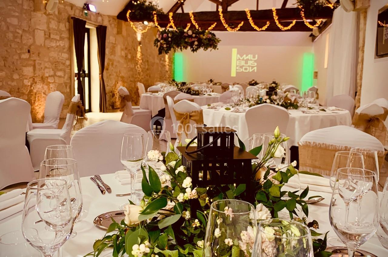 Salle de réception décorée avec des guirlandes lumineuses, des tables dressées et des compositions florales élégantes.