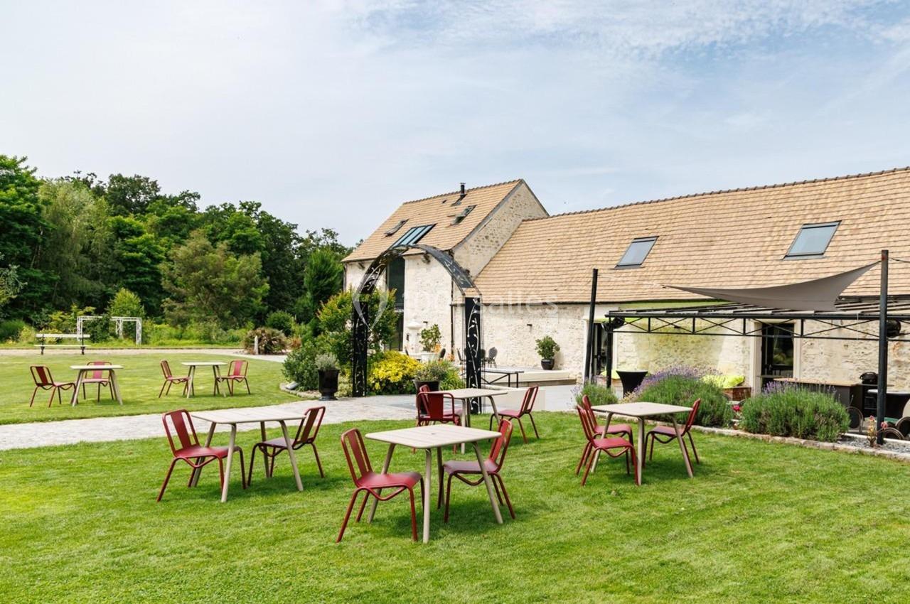 Tables et chaises disposées sur une pelouse devant un bâtiment en pierre avec toit en tuiles, par temps clair.