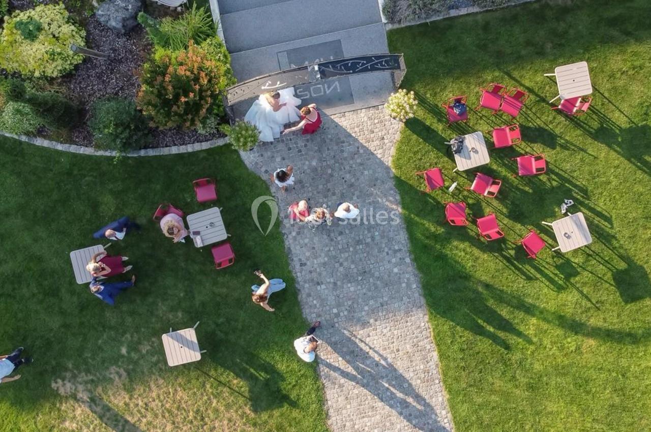 Vue aérienne d'un jardin avec des tables, des chaises rouges et des personnes rassemblées sur une allée pavée.