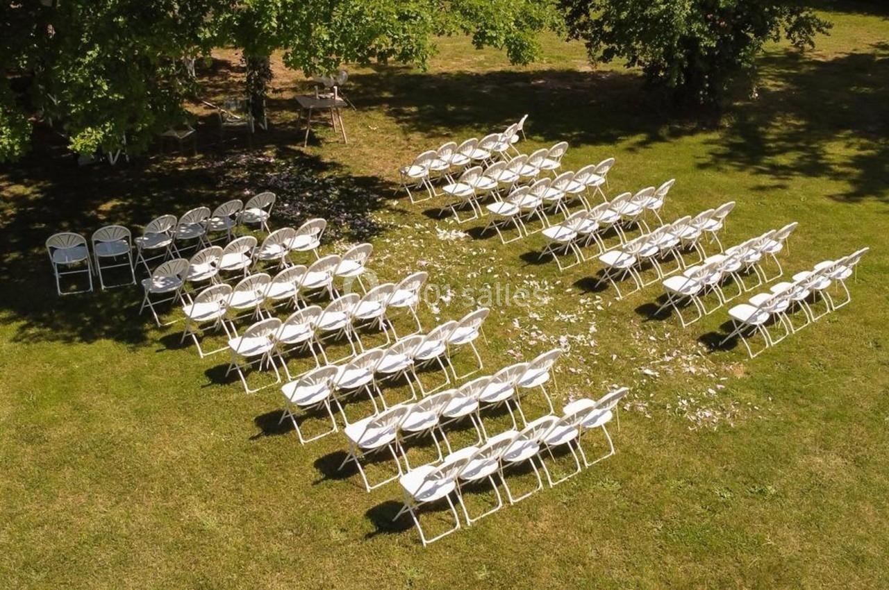 Chaises blanches disposées en rangées sur une pelouse, formant un espace pour un événement en extérieur.