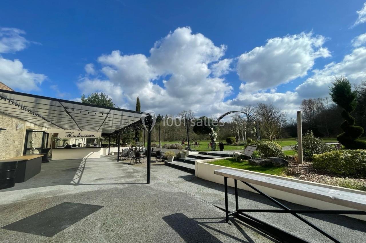 Terrasse aménagée avec pergola, mobilier extérieur et vue sur un jardin verdoyant sous un ciel partiellement nuageux.
