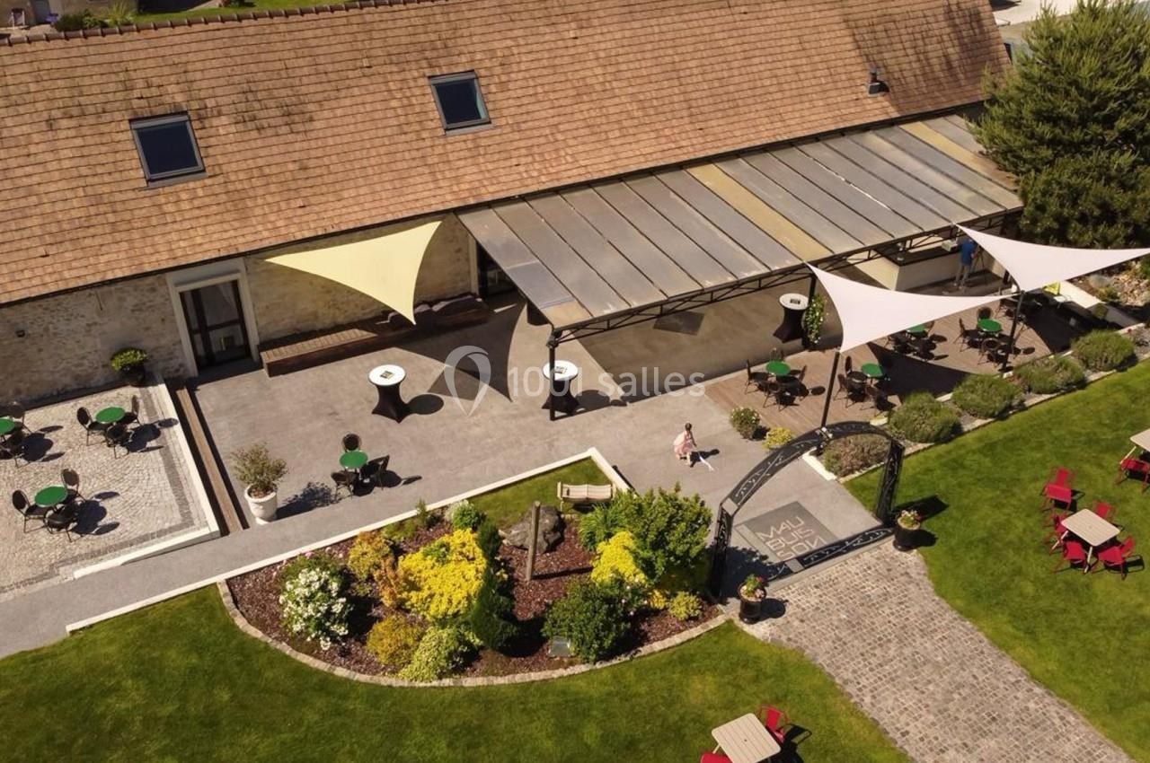 Vue aérienne d'une terrasse aménagée avec des tables, des parasols et un jardin paysager attenant.