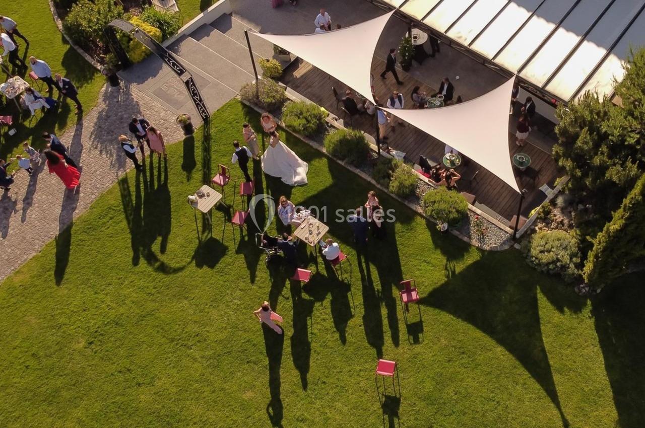 Vue aérienne d'un jardin avec des invités rassemblés près d'une terrasse couverte par des voiles d'ombrage.