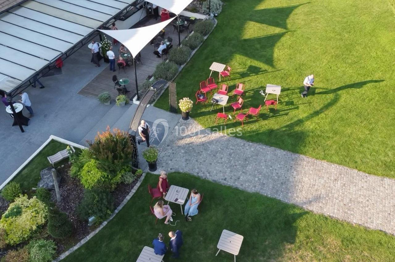 Vue aérienne d'un jardin avec des tables, des chaises rouges, des allées pavées et une terrasse couverte animée.