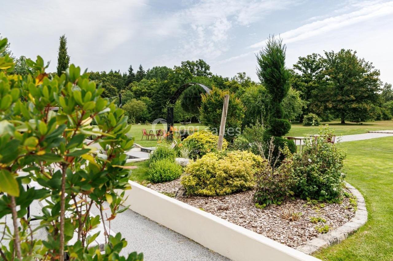 Jardin paysager avec arbustes, pelouse et mobilier de jardin sous une arche métallique, par temps clair.