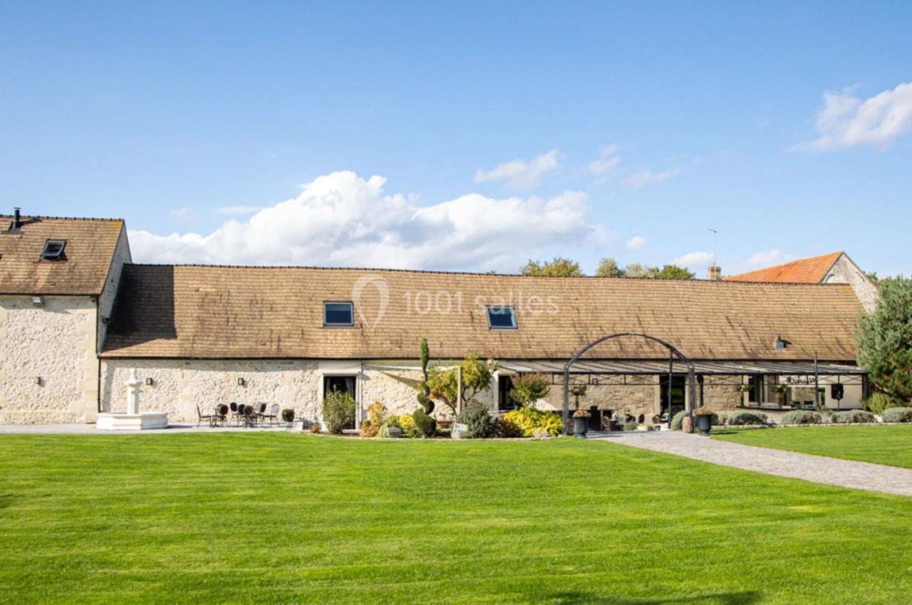 Bâtiment en pierre rénové avec toit en tuiles, entouré d'une pelouse et d'un ciel dégagé.