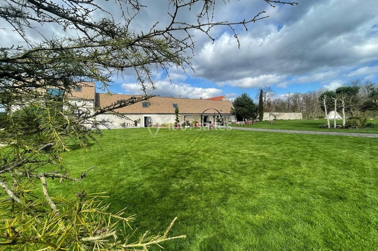 Pelouse verdoyante devant un bâtiment en pierre avec ciel partiellement nuageux et arbres en arrière-plan.