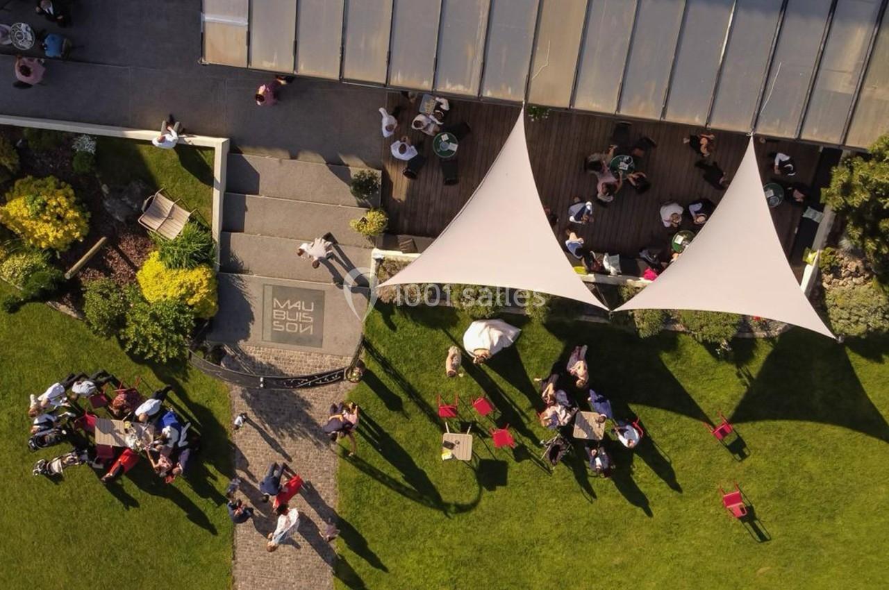 Vue aérienne d'une terrasse avec des voiles d'ombrage, des tables occupées et un jardin verdoyant environnant.