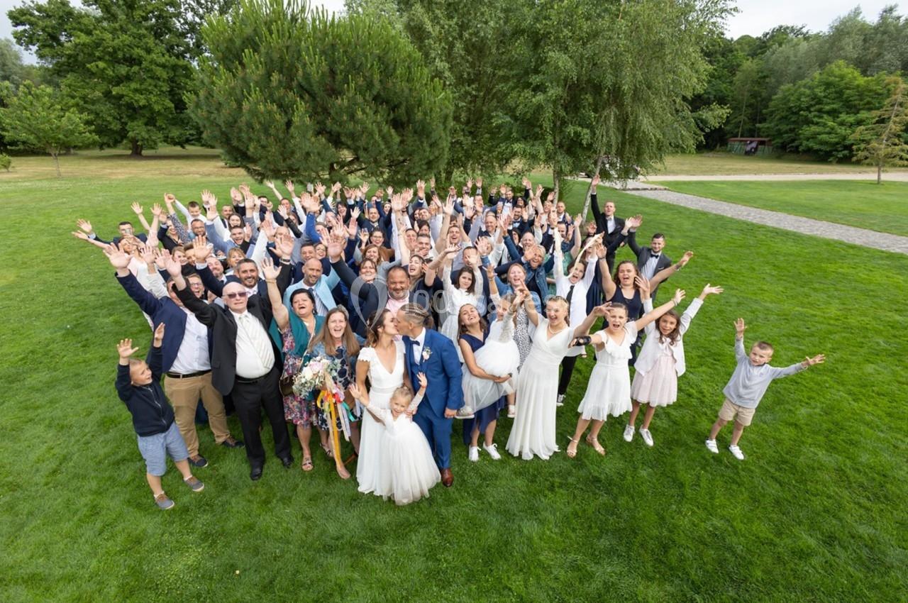 Groupe de personnes célébrant un mariage en plein air, souriants et levant les bras sur une pelouse verdoyante.