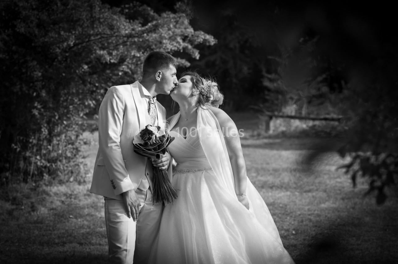 Un couple en tenue de mariage s'embrasse dans un jardin, avec des arbres en arrière-plan.