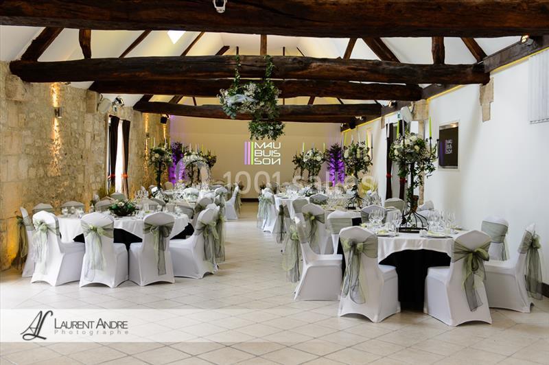 Salle de réception élégamment décorée avec des tables rondes, nappes blanches et chaises ornées de rubans verts.
