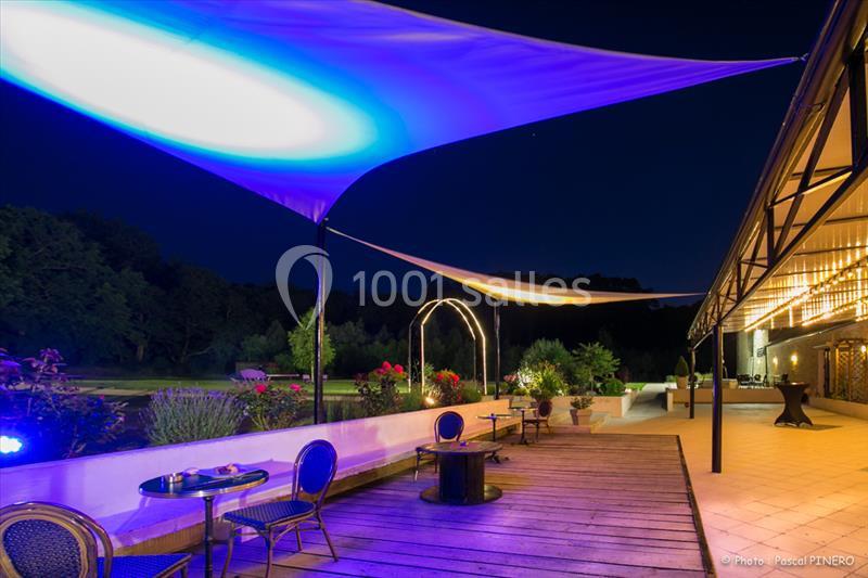 Terrasse en soirée avec voiles d'ombrage éclairées, mobilier de jardin et vue sur un espace naturel.