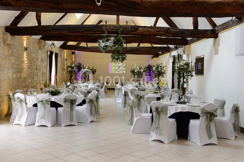 Salle de réception élégante avec tables dressées, chaises décorées de nœuds verts et poutres apparentes au plafond.