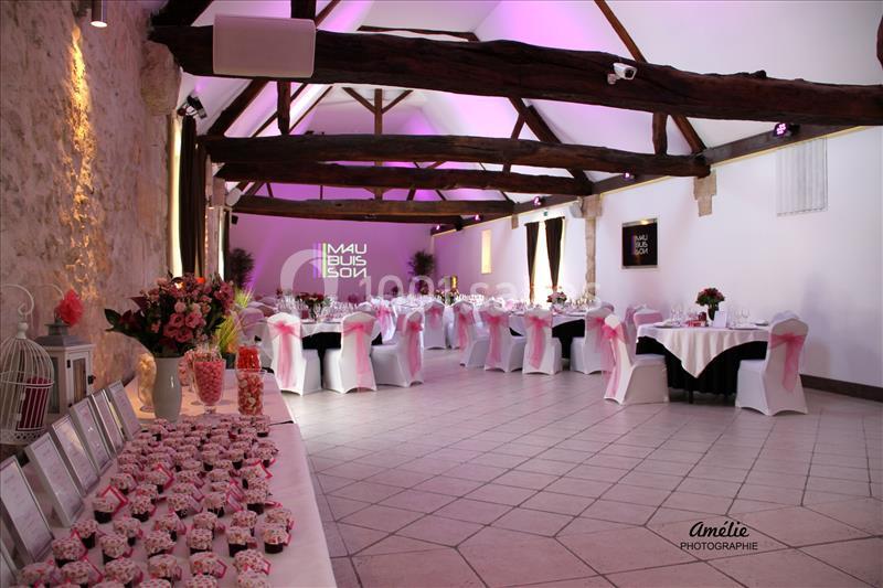 Salle de réception décorée avec des tables dressées, des chaises ornées de nœuds roses et un éclairage tamisé.
