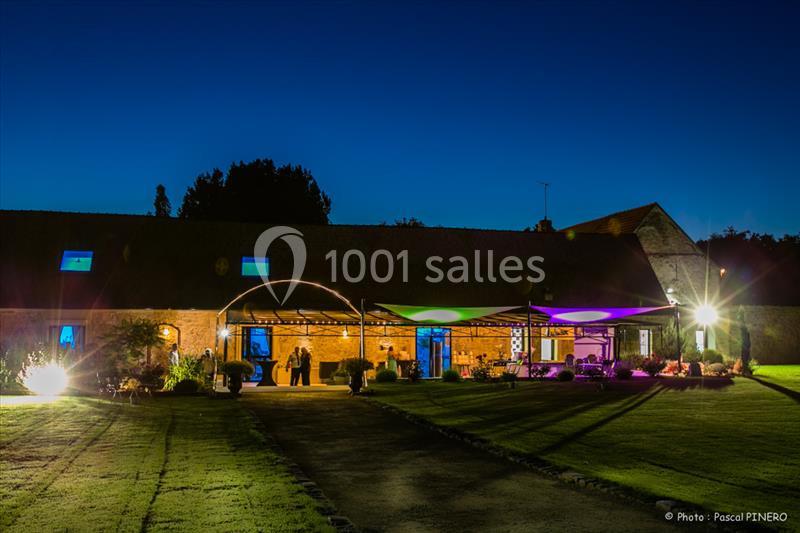 Bâtiment en pierre éclairé de nuit avec une terrasse couverte et un jardin aménagé au premier plan.