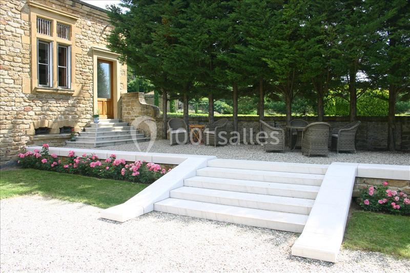Escalier en pierre blanche menant à une terrasse avec mobilier de jardin, entourée de haies et de fleurs roses.
