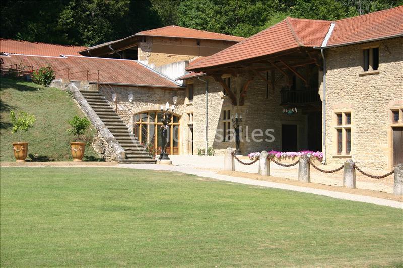 Bâtisse en pierre avec toit en tuiles, escalier extérieur, pelouse et pots décoratifs dans un cadre verdoyant.