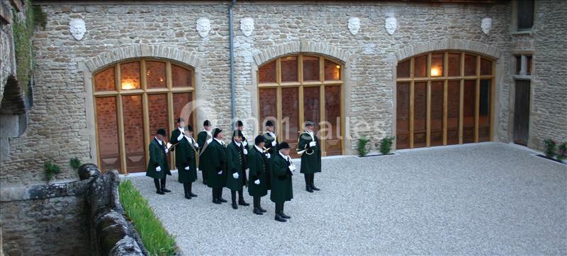 Un groupe de personnes en tenue traditionnelle se tient dans une cour pavée entourée de murs en pierre.
