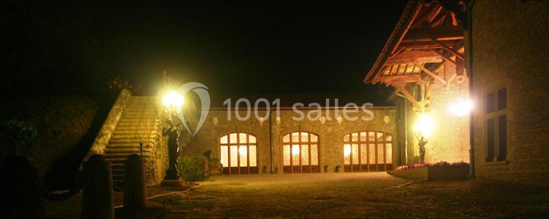 Façade éclairée d'un bâtiment en pierre avec des arches vitrées, de nuit, entourée d'escaliers et de végétation.