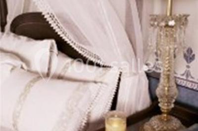 Lit avec baldaquin blanc, table de chevet en bois avec lampe en cristal, bougie et livres posés dessus.