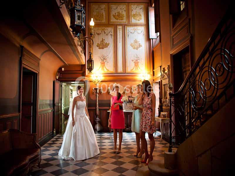 Une mariée en robe blanche discute avec trois femmes dans un hall élégant au sol en damier.