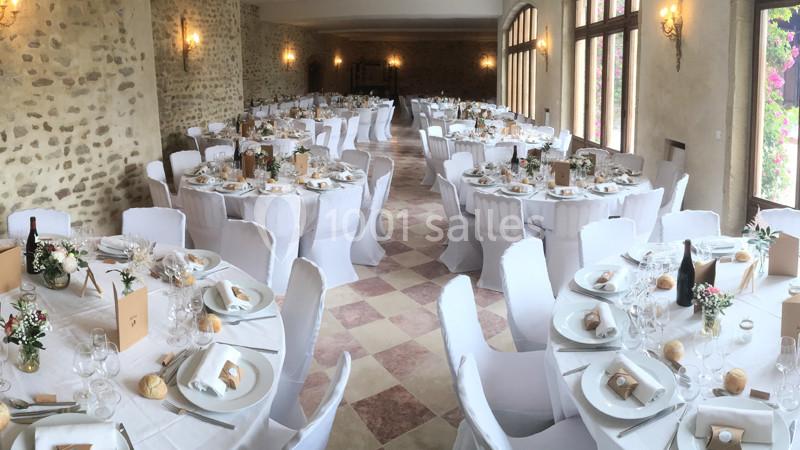 Salle de réception décorée pour un événement, avec des tables rondes dressées et des chaises blanches.