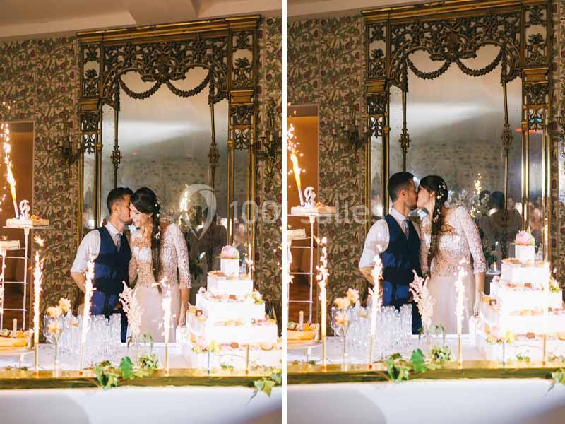 Un couple de mariés s'embrasse devant une table décorée avec un gâteau de mariage et des étincelles.