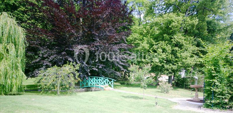 Petit pont en bois turquoise traversant un ruisseau dans un parc verdoyant avec arbres et pelouse.