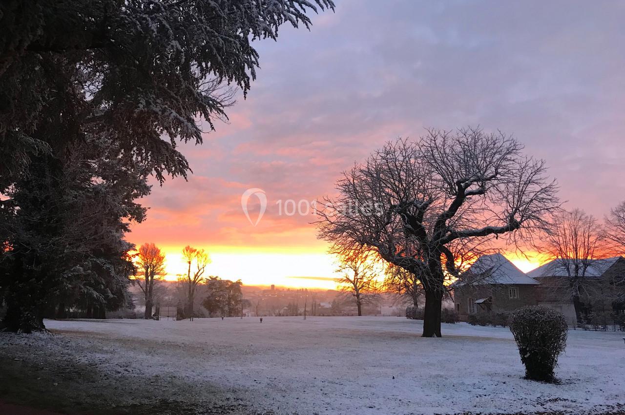 Paysage hivernal avec un coucher de soleil coloré, des arbres dénudés et un sol légèrement recouvert de neige.