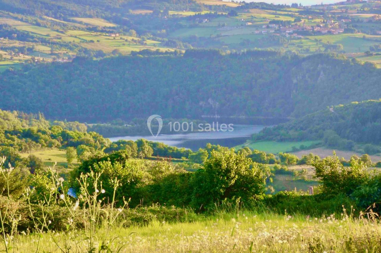 Paysage vallonné avec un lac entouré de forêts et de prairies verdoyantes sous une lumière douce.