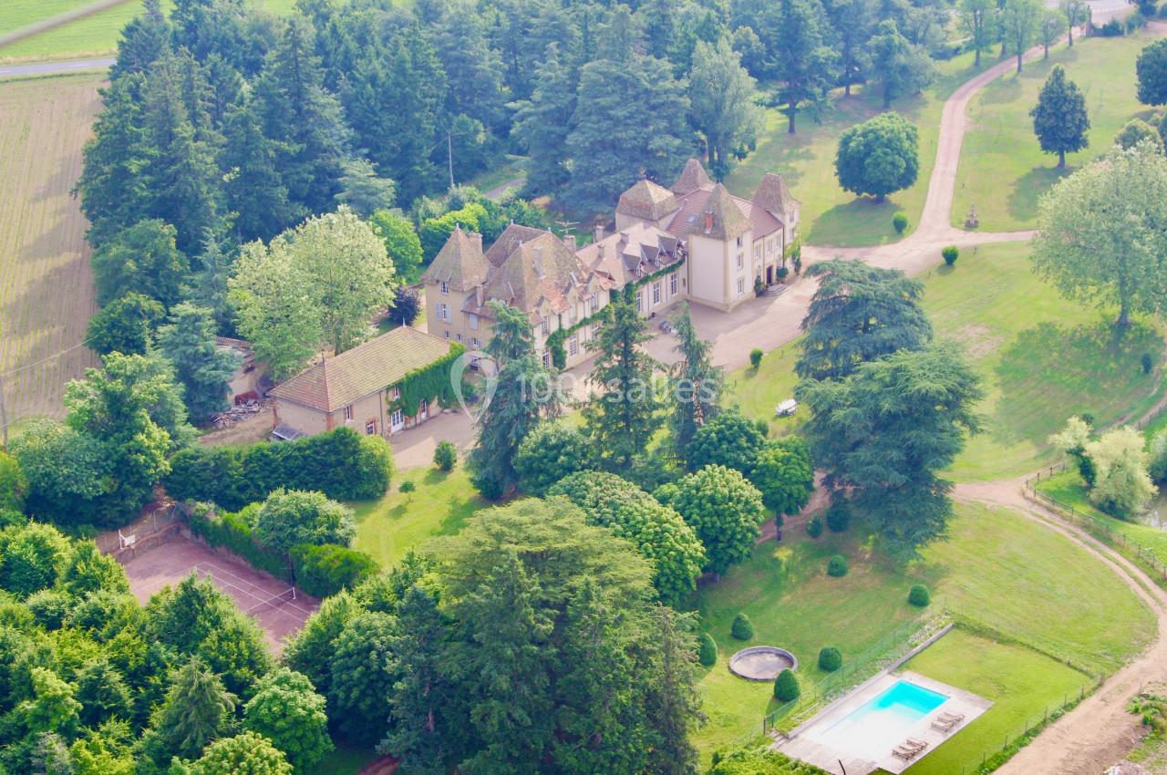 Vue aérienne d'un domaine avec un château entouré de jardins, arbres, piscine et chemins en pleine campagne.