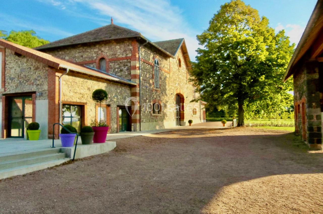 Bâtiment en pierre avec des pots colorés devant, entouré d'arbres et baigné de lumière naturelle.