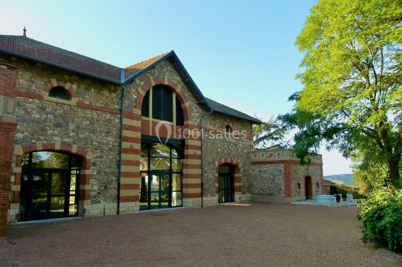 Bâtiment en pierre et briques rouges avec grandes fenêtres, entouré d'arbres et d'une cour en gravier.