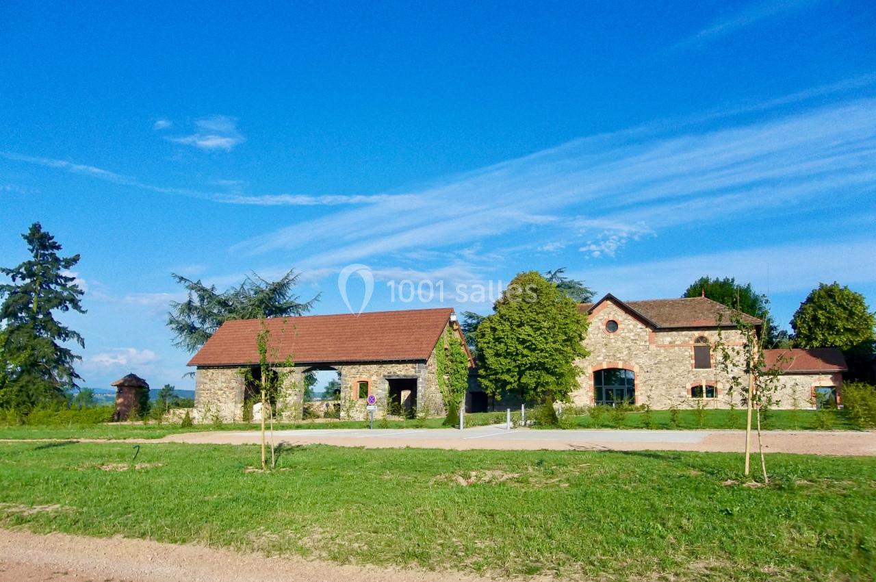 Bâtiments en pierre avec toits en tuiles rouges entourés de pelouse et d'arbres sous un ciel bleu dégagé.
