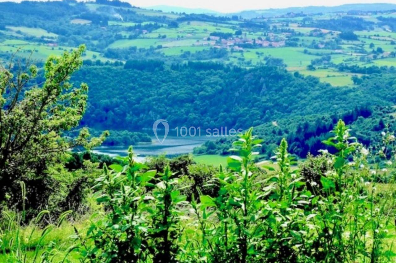 Paysage vallonné avec végétation dense au premier plan, rivière sinueuse et villages dispersés à l'horizon.