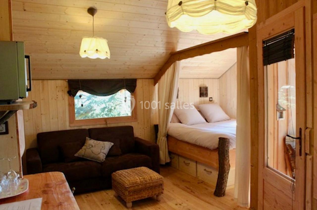 Intérieur d'une cabane en bois avec un canapé, un lit double, des luminaires suspendus et une ambiance chaleureuse.