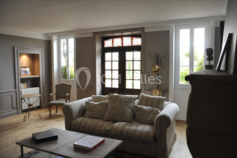 Salon lumineux avec canapé beige, table basse, porte-fenêtre en bois, et décoration sobre dans un style classique.