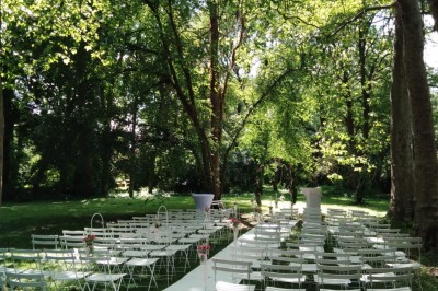 Disposition de chaises blanches en extérieur autour d'une allée menant à une petite scène sous une tente blanche.