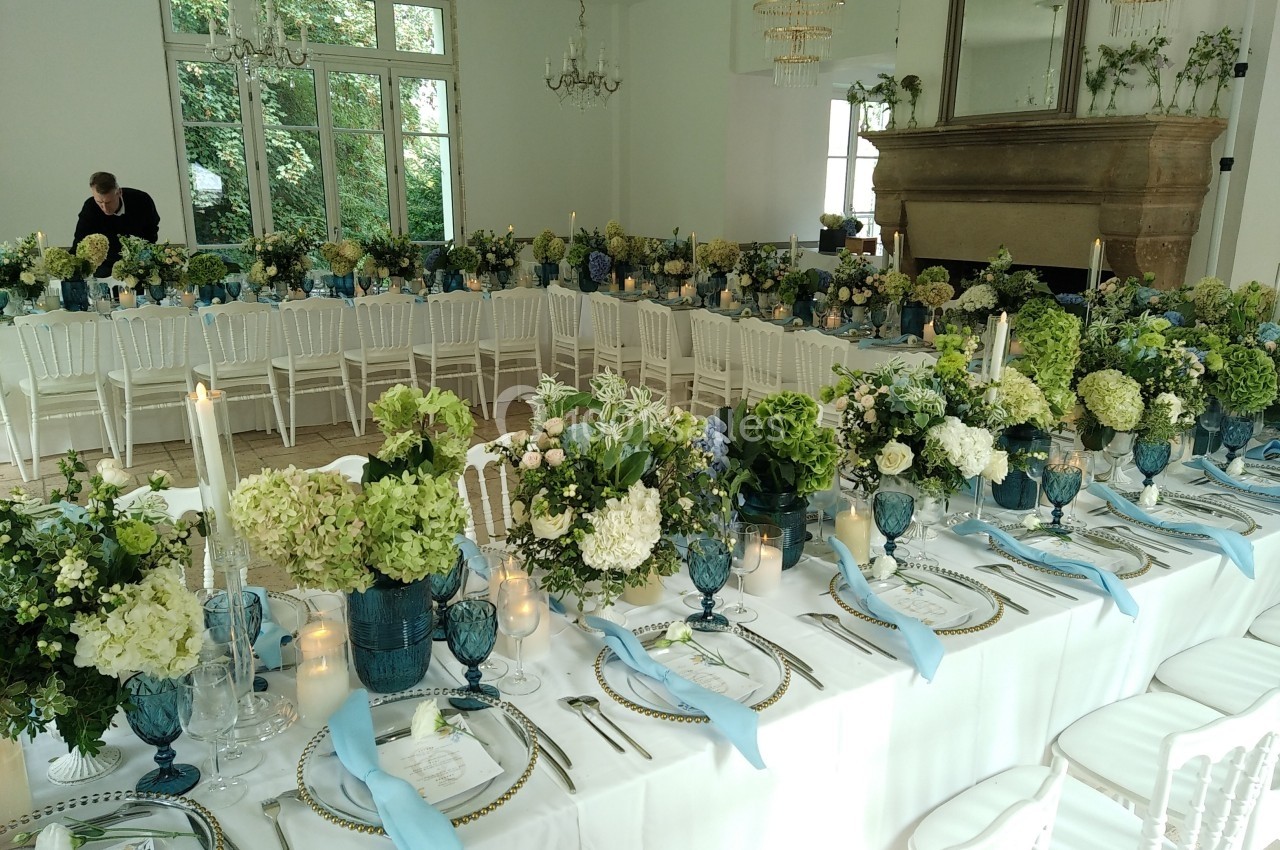 Salle de réception décorée avec des tables élégantes, nappes blanches, fleurs et vaisselle raffinée.