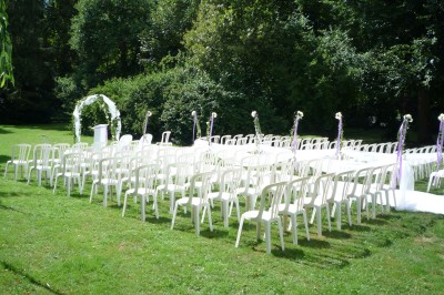 Disposition de chaises blanches en extérieur autour d'une allée menant à une petite scène sous une tente blanche.