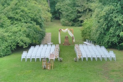 Disposition de chaises blanches en extérieur autour d'une allée menant à une petite scène sous une tente blanche.
