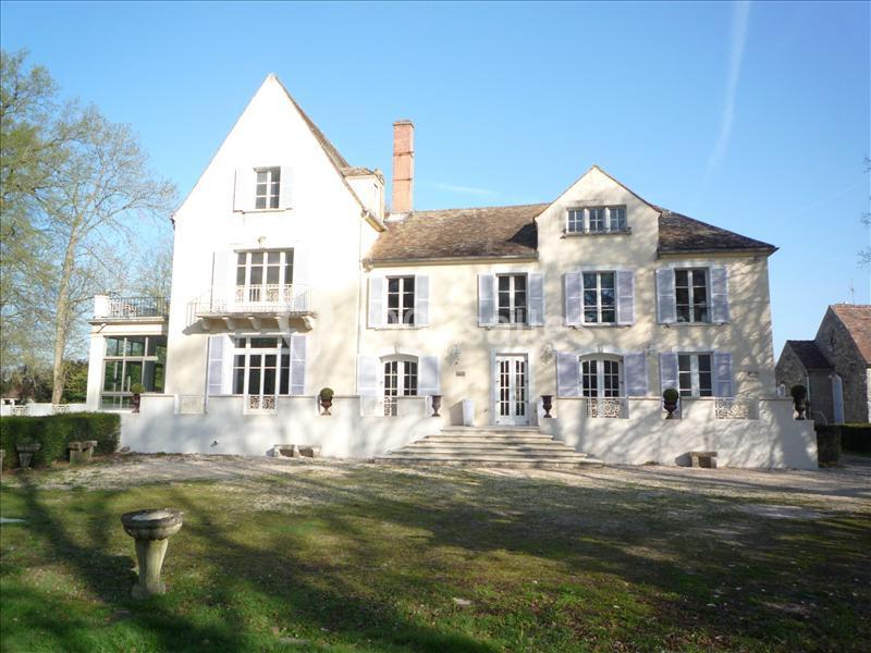Façade d'une grande maison de campagne en pierre claire, entourée d'arbres et d'une pelouse.
