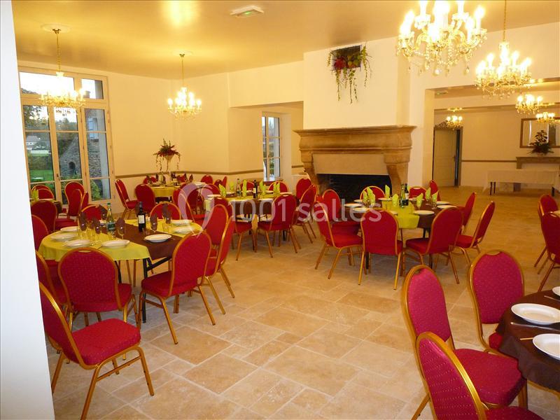 Salle de réception lumineuse avec tables dressées, chaises rouges et lustres suspendus.