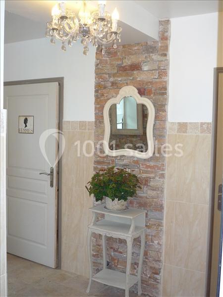 Un miroir encadré au-dessus d'une table avec une plante, près d'un mur en briques et une porte marquée ’Femmes’.