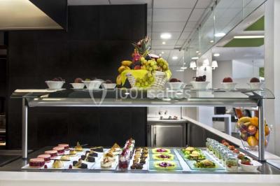 Vue aérienne d'un bâtiment en forme de cour rectangulaire avec des toits en tuiles, entouré de champs et d'arbres.