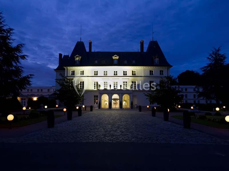 Façade éclairée d'un bâtiment historique avec toit mansardé, vue de nuit sur une allée pavée et des lampes sphériques.